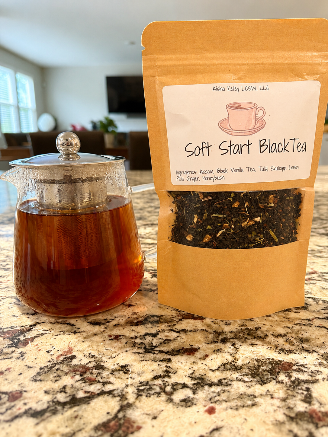 Tea bag packaging labeled 'Soft Start Black Tea' next to a glass teapot with tea on a marble surface.